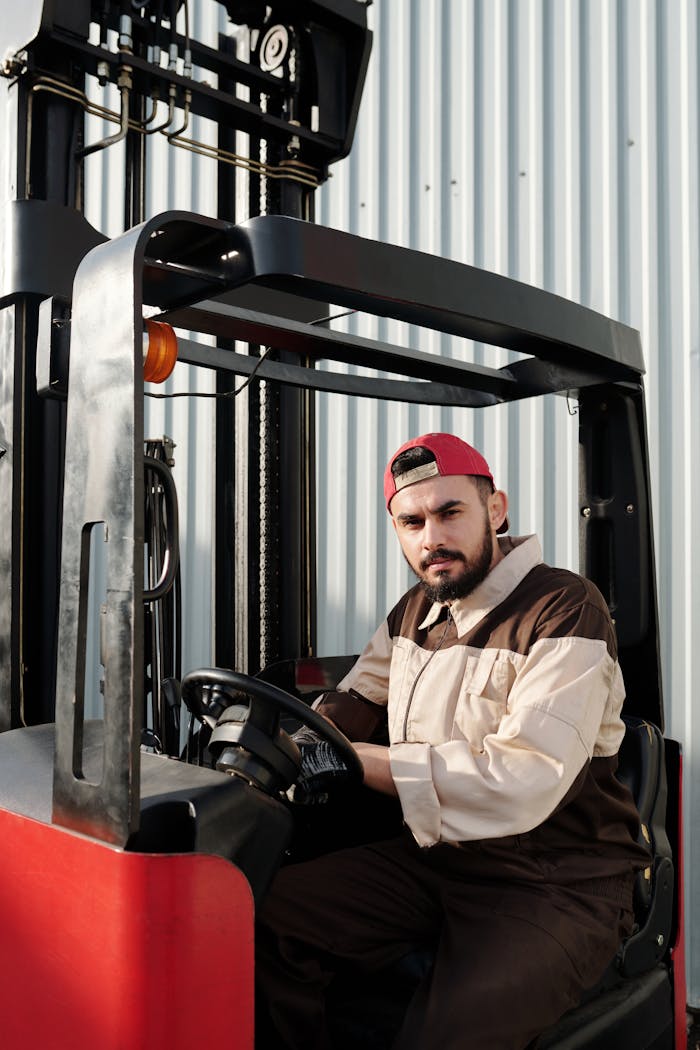 Services-02 Portrait of a forklift operator inside a warehouse, wearing a uniform and cap.