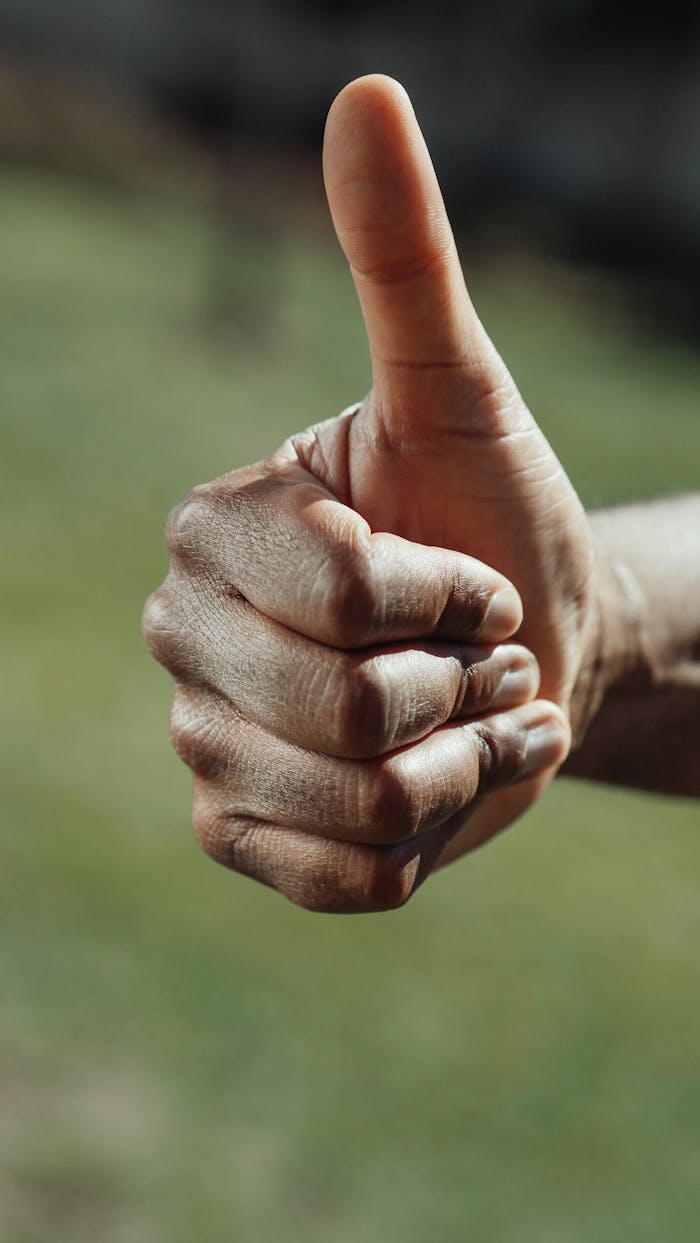 Detailed close-up of a hand giving a thumbs up gesture in natural light.