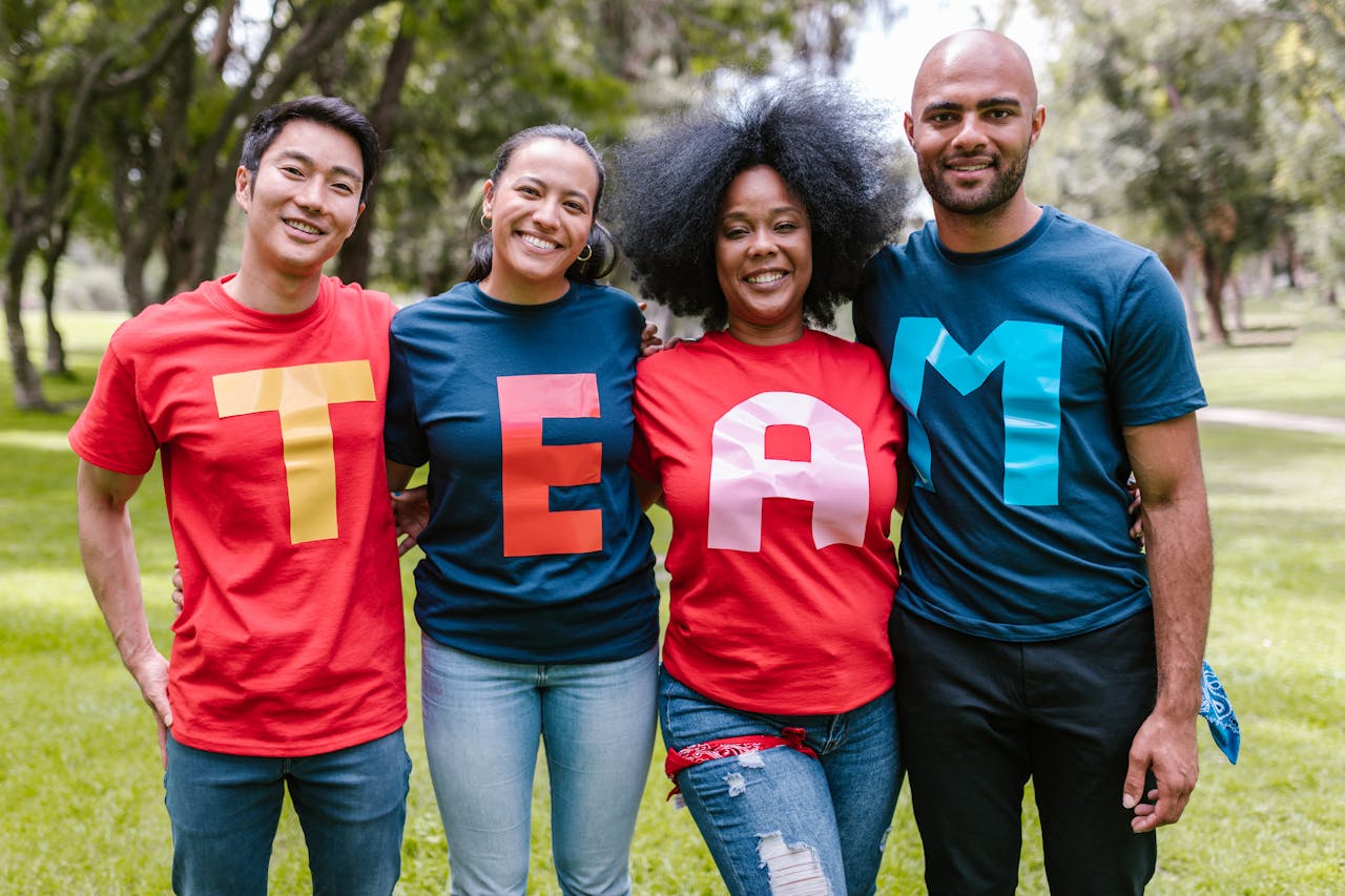 creative-03 A diverse group of adults bonding and smiling in a park wearing TEAM shirts.